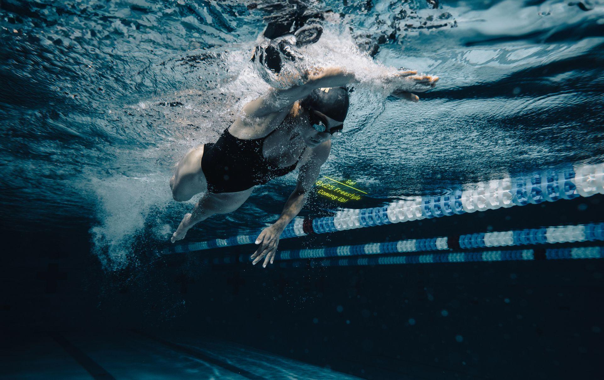 Underwater view of a swimmer in a black swimsuit performing a freestyle stroke in a swimming pool.